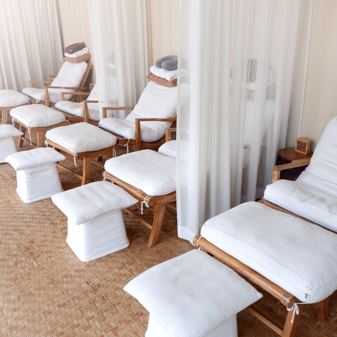 4 wooden recliner chairs with white cushions and a white ottoman are lined up in a spa.