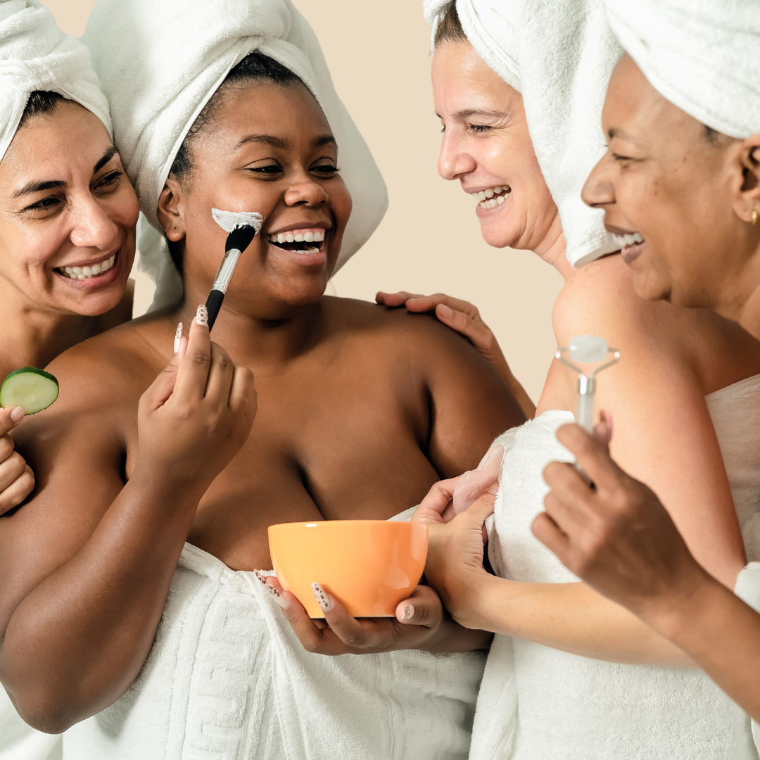 Four women of wrapped in towels and turbans in a spa environment, smile into the camera. The women are from diverse backgrounds, showcasing racial diversity and body diversity. They are part of an inclusive marketing campaign for spas.